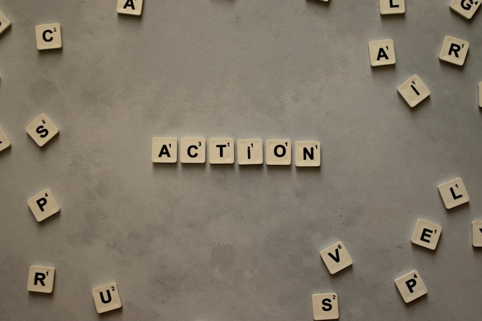 Flat lay of Scrabble tiles spelling 'Action' on a gray background, surrounded by random letters.